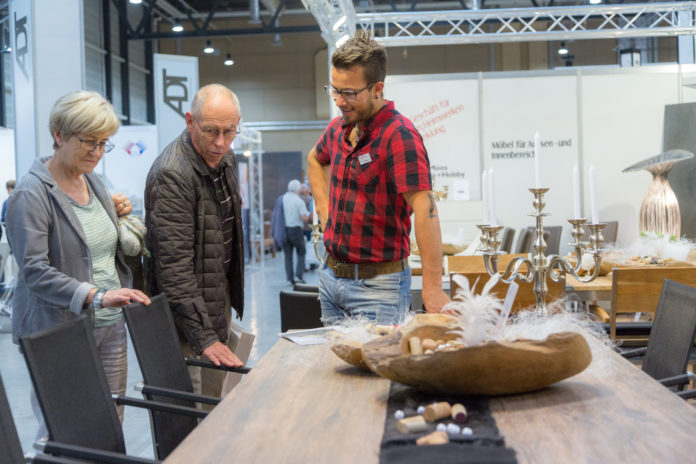 Ein Aussteller zeigt einem Besucher einen Tisch an einer Ausstellung.