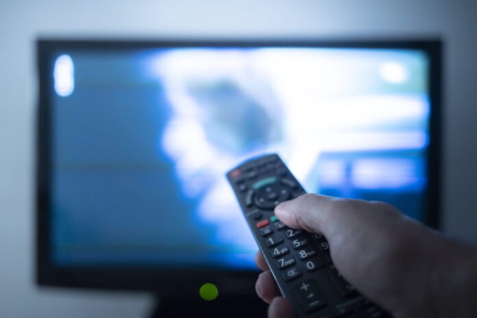 Hand with remote control in front of the tv Quelle: Omdia.